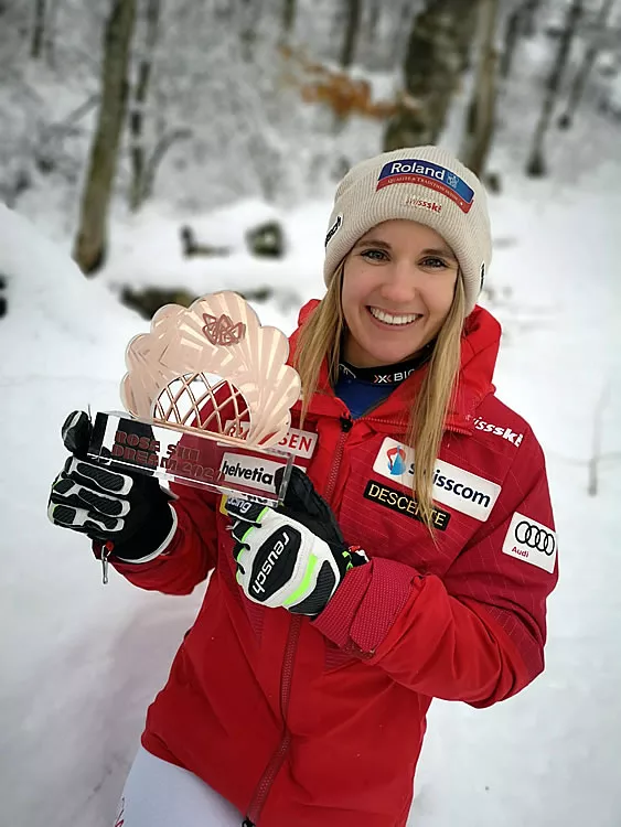 Joana Hählen im Schnee mit Kristallkugel-Trophäe, lachend in rotem Swiss-Ski-Rennanzug